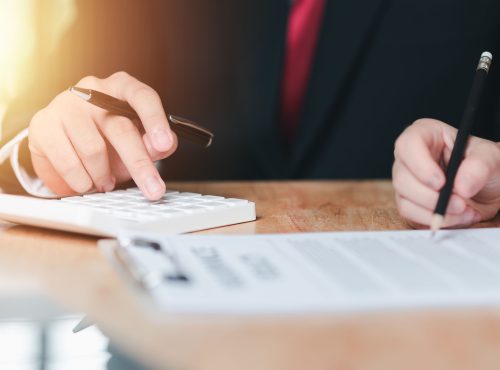 Hands of business professionals using calculator and signing contract at Pioneer Business Brokers.